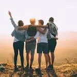 A group of friends embrace while enjoying a sunset view from the mountain top.