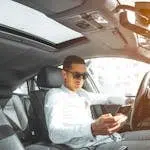 A man wearing sunglasses texts on his phone while driving a car in Morocco.